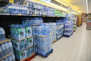 Zdjęcie przedstawia alejkę w sklepie z wystawionymi butelkami wody mineralnej na półkach.