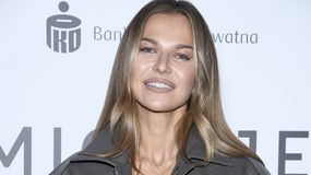 Na zdjęciu uśmiechnięta Anna Lewandowska w szarej kurtce, z długimi, falującymi włosami.