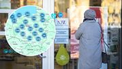 Kobieta w szarym płaszczu przy wejściu do placówki NFZ, patrzy na plakat informacyjny.