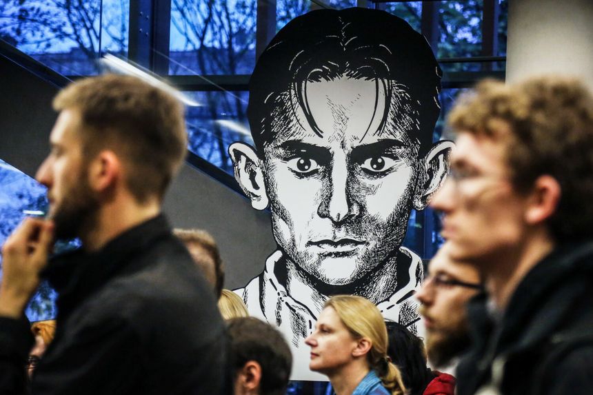 Grupa ludzi na tle dużego portretu w stylu graficznym, przedstawiającego mężczyznę.