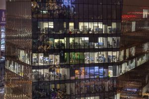 Szklany budynek biurowy nocą, widać oświetlone pomieszczenia z biurkami.