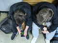 Dwa chłopcy w czarnych bluzach siedzą na ławce, jeden trzyma telefon, grając w grę.
