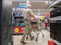 Mężczyzna w koszuli w kratę pcha wózek sklepowym w supermarkecie z hasłem 