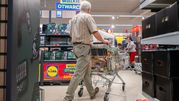 Mężczyzna w koszuli w kratę pcha wózek sklepowym w supermarkecie z hasłem 