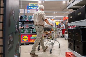 Mężczyzna w koszuli w kratę pcha wózek sklepowym w supermarkecie z hasłem 