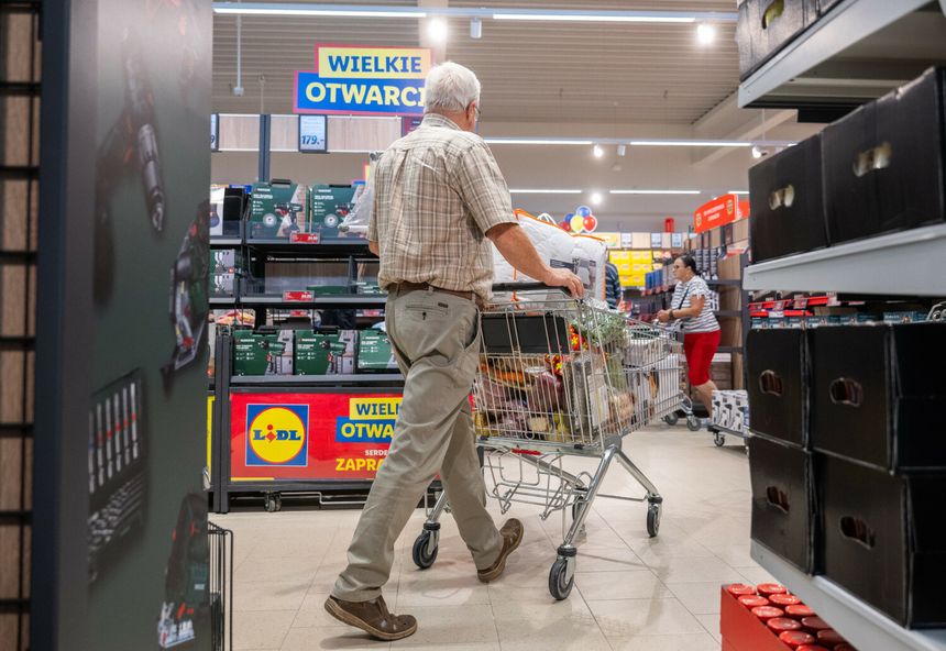 Mężczyzna w koszuli w kratę pcha wózek sklepowym w supermarkecie z hasłem 