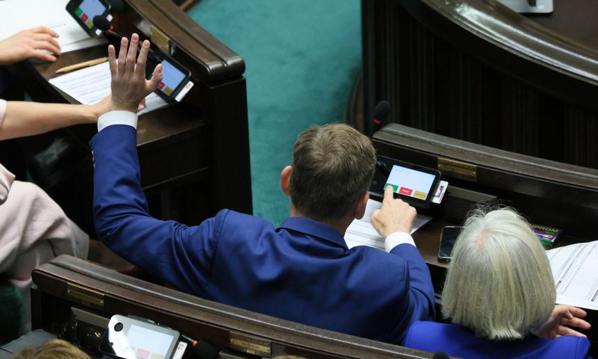 Na zdjęciu widoczna jest osoba w niebieskim garniturze, głosująca w Sejmie.