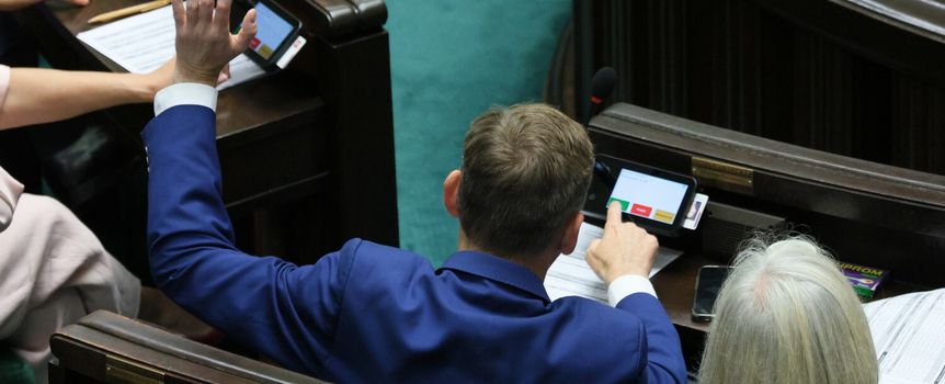Na zdjęciu widoczna jest osoba w niebieskim garniturze, głosująca w Sejmie.
