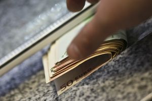 Zbliżenie na rękę trzymającą pieniądze w euro, na tle kamiennego blatu.