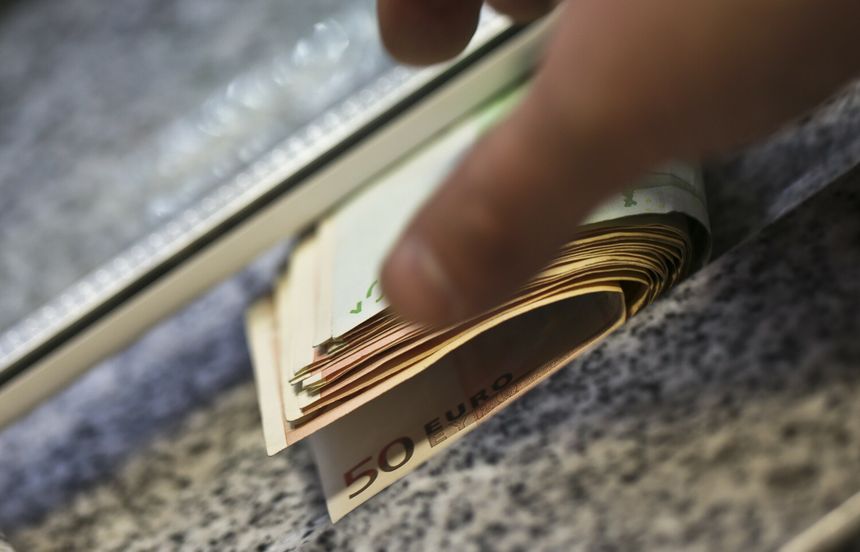 Zbliżenie na rękę trzymającą pieniądze w euro, na tle kamiennego blatu.