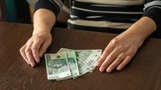 Na stole leżą polskie banknoty. Dwie ręce osoby trzymają pieniądze.
