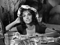 Gina Lollobrigida. Kobieta w ciemnej bluzce, otoczona banknotami, patrzy z uśmiechem w stronę obiektywu.