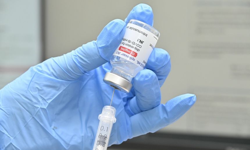Ręka w niebieskiej rękawiczce trzyma fiolkę szczepionki z igłą do pobrania dawkowania.