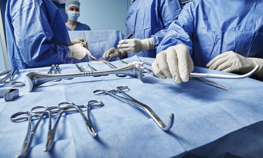 Zdjęcie przedstawia chirurgów w niebieskich strojach, pracujących w sali operacyjnej.