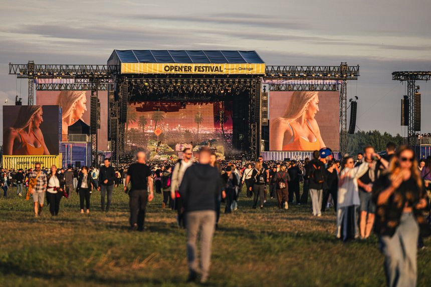 Tłum ludzi na festiwalu Open'er, widok na scenę z dużymi ekranami.