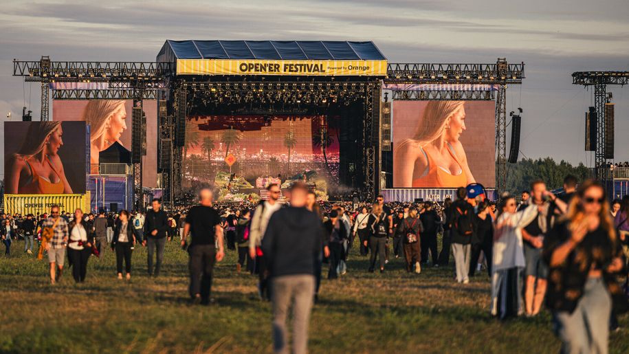 Tłum ludzi na festiwalu Open'er, widok na scenę z dużymi ekranami.
