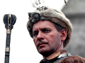 Mężczyzna w futrzanej czapce, trzymający berło, w tle zamek. Historyczny lub filmowy motyw.