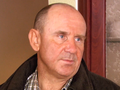 Mężczyzna z jasno niebieskimi oczami, w ciemnej kurtce, o krótkich włosach, stoi w pomieszczeniu.