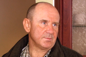 Mężczyzna z jasno niebieskimi oczami, w ciemnej kurtce, o krótkich włosach, stoi w pomieszczeniu.