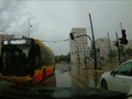 Na zdjęciu żółto-czarny autobus na ulicy w deszczowej pogodzie, obok stoi biały samochód.
