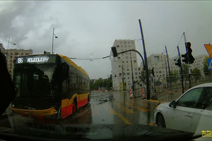 Na zdjęciu żółto-czarny autobus na ulicy w deszczowej pogodzie, obok stoi biały samochód.