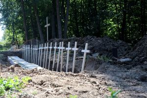 Grób z drewnianymi krzyżami w lesie, otoczony ziemią i zaroślami. 
