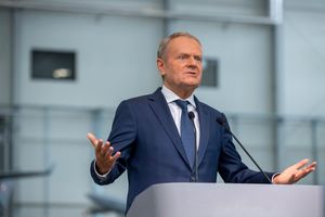 Mężczyzna w garniturze przemawia przy mównicy razem z mikrofonami w tle. Donald Tusk.
