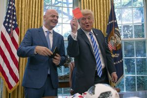 Na zdjęciu dwóch mężczyzn w garniturach. Jeden z nich trzyma czerwony karton, drugi się uśmiecha.