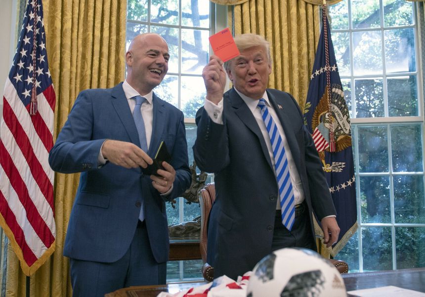 Na zdjęciu dwóch mężczyzn w garniturach. Jeden z nich trzyma czerwony karton, drugi się uśmiecha.