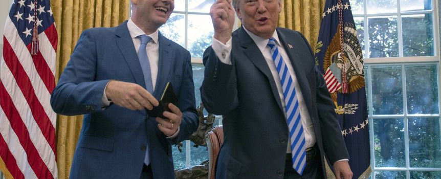 Na zdjęciu dwóch mężczyzn w garniturach. Jeden z nich trzyma czerwony karton, drugi się uśmiecha.