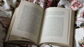 Otwarte książki na kwiecistej pościeli, tekst widoczny na stronach, spokojna atmosfera.