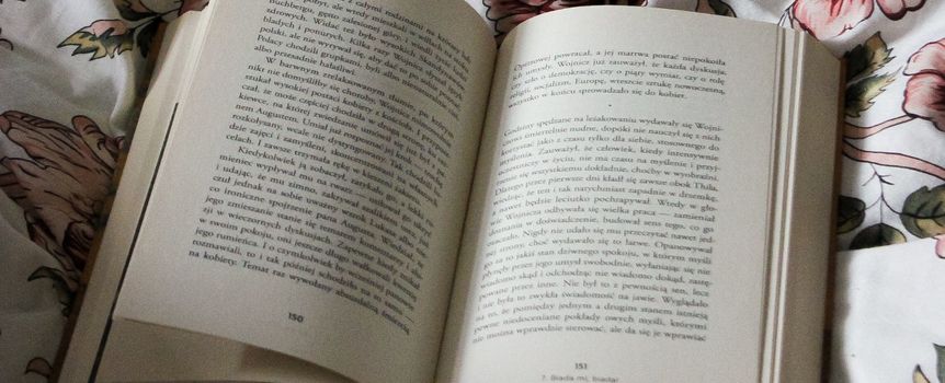 Otwarte książki na kwiecistej pościeli, tekst widoczny na stronach, spokojna atmosfera.