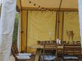Zielony las, przygotowany stół w namiocie, drewniane krzesła, dekoracje z naturalnych elementów.