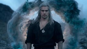 Mężczyzna z długimi, siwymi włosami, w czarnej koszuli, stoi przed magiczną chmurą.