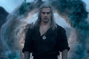 Mężczyzna z długimi, siwymi włosami, w czarnej koszuli, stoi przed magiczną chmurą.