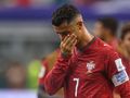 Cristiano Ronaldo w czerwonym stroju z logo Portugalii, smutny po przegranej. Wygląda na rozczarowanego.