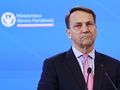 Mężczyzna w garniturze, z poważnym wyrazem twarzy, przemawia na konferencji.