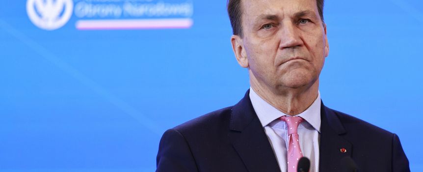 Mężczyzna w garniturze, z poważnym wyrazem twarzy, przemawia na konferencji.