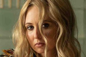Kobieta z falującymi blond włosami, z wyrazem smutku na twarzy, patrzy w dal.