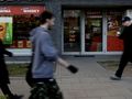 Na zdjęciu widoczni są przechodnie obok sklepu alkoholowego z dużą witryną.