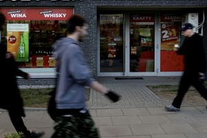 Na zdjęciu widoczni są przechodnie obok sklepu alkoholowego z dużą witryną.