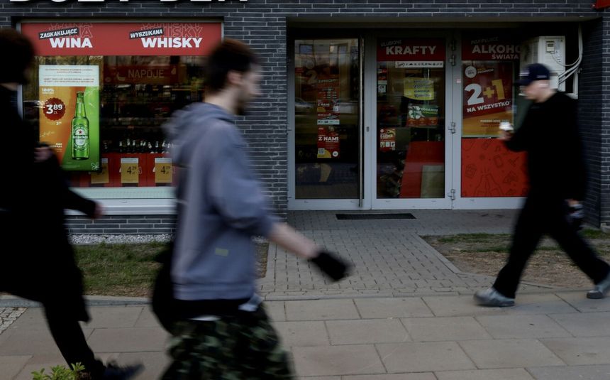 Na zdjęciu widoczni są przechodnie obok sklepu alkoholowego z dużą witryną.