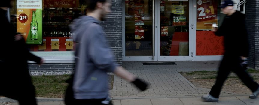 Na zdjęciu widoczni są przechodnie obok sklepu alkoholowego z dużą witryną.
