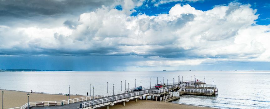 Widok na plażę i molo przy morzu, pod niebem pełnym chmur. Spokój i cisza.