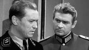 Na zdjęciu dwóch mężczyzn w mundurach wojskowych, jeden w uniformie SS, z poważnymi minami.