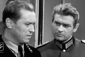 Na zdjęciu dwóch mężczyzn w mundurach wojskowych, jeden w uniformie SS, z poważnymi minami.