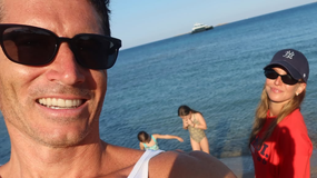 Robert Lewandowski w okularach przeciwsłonecznych z uśmiechem, obok Anna Lewandowska i dzieci w wodzie.