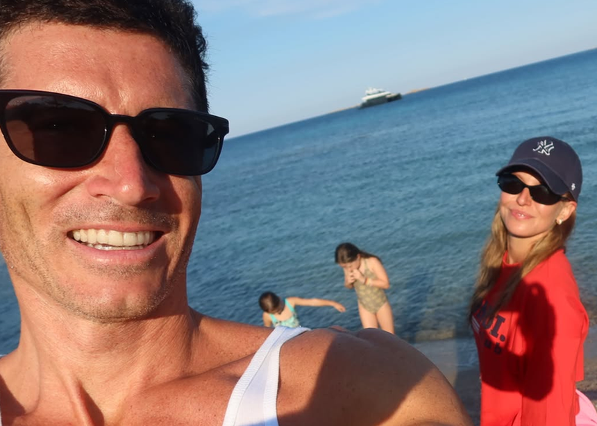 Robert Lewandowski w okularach przeciwsłonecznych z uśmiechem, obok Anna Lewandowska i dzieci w wodzie.