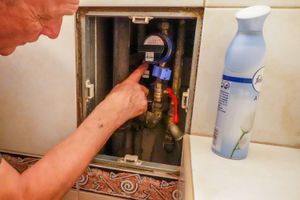 Mężczyzna sprawdza wodomierz w łazience, obok widoczny spray zapachowy.