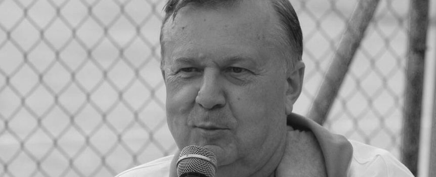 Karol Stopa z mikrofonem w ręku, ubrany w biały T-shirt, z siatką w tle.